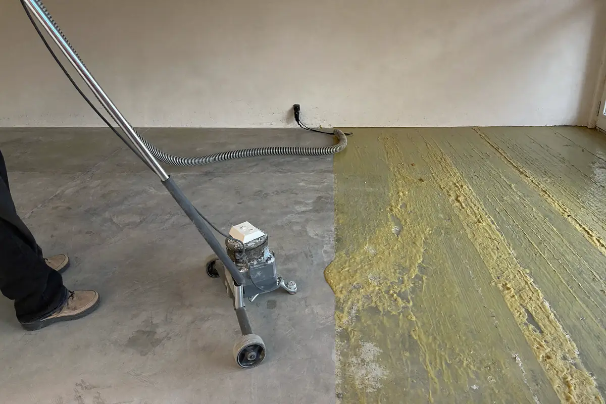 Vloerfrees met stofafzuiging die oude lijmresten van een betonnen dekvloer wegslijpt, half schoon en half nog met lijm