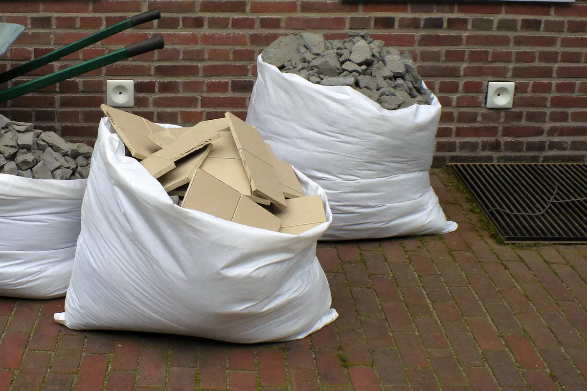 Gevulde big bags met gebroken tegels en dekvloerpuin op de oprit voor een bakstenen rijwoning