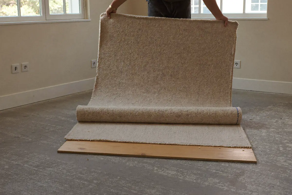 Oud beige tapijt dat in een lege slaapkamer wordt opgerold, met spijkerlatten langs de plint